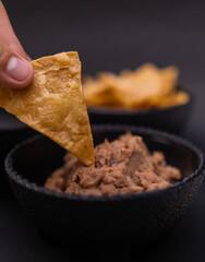 Hand dipping tortilla chip in bowl of refried beans