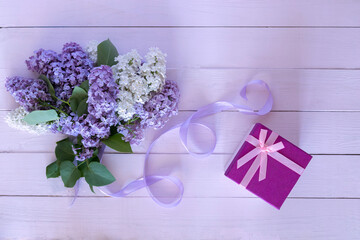A bouquet of lilac and white flowers with a ribbon and a pink gift box on a pink background. A holiday card. Floral background.I congratulate you on the holiday. Mother's Day, Teacher's Day, March 8.