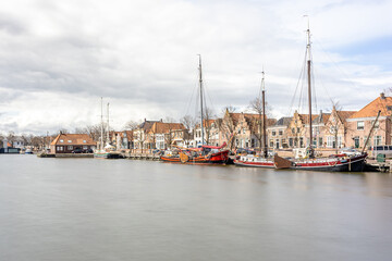 Fototapeta na wymiar Oosterhaven quay in the city harbor, anchored boats, houses and buildings in the background, cloudy day with stormy clouds in Medemblik, Noord-Holland, Netherlands. Long exposure photography