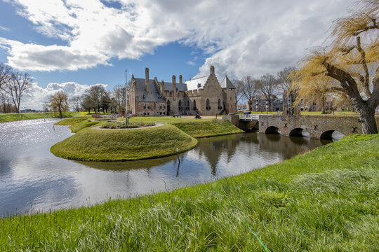Picturesque landscape with Radboud castle surrounded by its moat in the background, brick walls, bridges, bare trees, calm day with a blue sky and white clouds in Medemblik, Noord-Holland, Netherlands