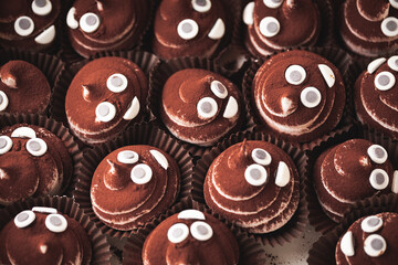 Set of cupcakes in the white gift box. Chocolate cupcake with brown whipped marshmallow top decorated with mastic smiley face and sprinkled with cocoa powder