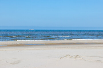 Empty brown sand beach with a boat sailing in the sea in the background, sunny spring day with a clear blue sky at Petten aan Zee, Noord-Holland in the Netherlands