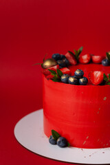Red cake with cream cheese frosting for a big event. luxurious cake with golden decoration and berries on top on the red background