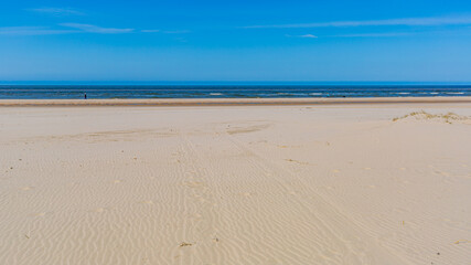 Wide beach with brown sand with people walking in the distance with the sea in the background, sunny spring day with a clear blue sky at Petten aan Zee, Noord-Holland in the Netherlands