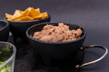 Bowls of tortilla chips, refried beans, and chopped lettuce on Mexican comal