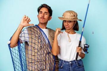 Young mixed race fisher couple isolated on blue background feels proud and self confident, example to follow.