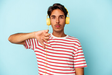 Young mixed race man listening to music isolated on blue background showing a dislike gesture,...