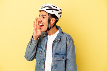 Young mixed race man wearing a helmet bike isolated on yellow background shouting and holding palm near opened mouth.