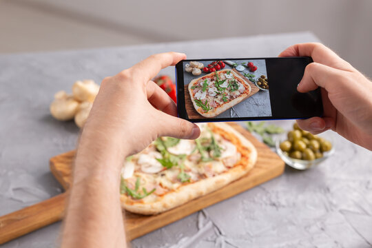 Chef takes pictures of the cooked of italian pizza with parma ham on smartphone. Photographing food and social networks concept.