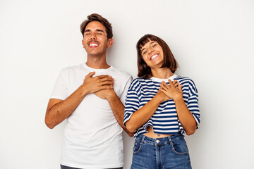 Young mixed race couple isolated on white background laughing keeping hands on heart, concept of happiness.