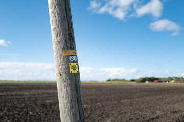  Leaning wooden telegraph pole in a rural location, near a distant farm. The pole advertises that it carries Fibre Optic Internet Broadband to a rural community - obrazy, fototapety, plakaty