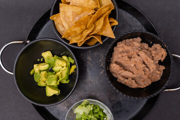 Bowls of tortilla chips, refried beans, and chopped avocado on Mexican comal