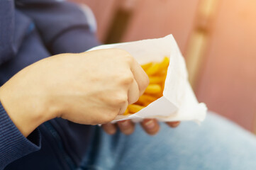 A woman's hand with delicious French fries in a paper bag on a light background. French fries. A woman's hand takes a potato out of a paper bag. Fast food. Greasy, unhealthy food.
