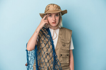 Young caucasian fisherwoman holding a net isolated on blue background showing a disappointment...