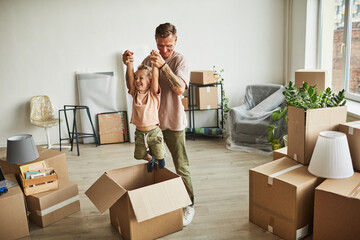 Portrait of happy father playing with son in cardboard boxes while family moving to new house, copy...
