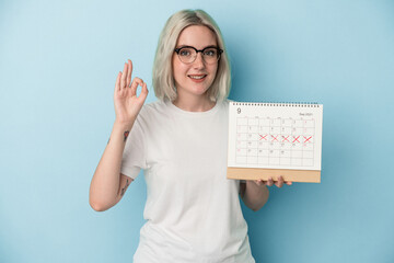 Young caucasian woman holding calendar isolated on blue background cheerful and confident showing...