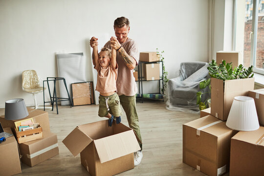 Portrait of happy father playing with son in cardboard boxes while family moving to new house, copy space