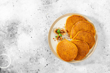 Pumpkin pancakes in a ceramic plate on a light gray culinary background with top view