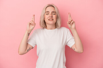 Young caucasian woman isolated on pink background crossing fingers for having luck