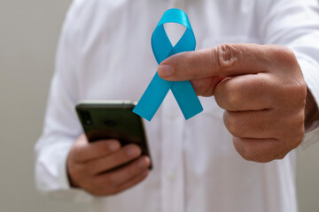 man in white shirt holding blue ribbon and cellphone. Blue november. Prostate Cancer Prevention Month. Men's health.