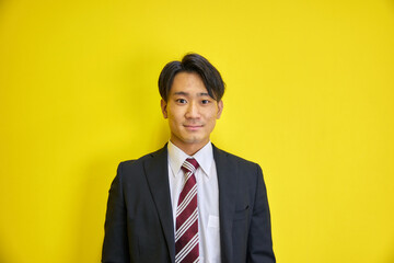 黄色い背景の前で爽やかに笑うスーツを着た日本人男性