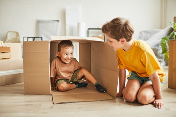Portrait of two brothers playing with cardboard box while family moving to new house, copy space