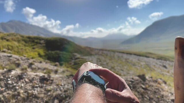 Closeup of a man wears and uses a smartwatch outdoor in the mountain. Lens flare. Ready to workout. Technology.