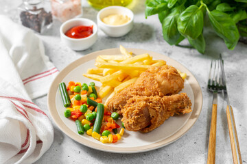 Fried crispy chicken legs in breadcrumbs with french fries and vegetables in a plate on a culinary background. Fast food from the drumstick close-up	