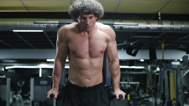 Man exercising on parallel bars. Young athlete exercising in gym. Steadicam shot zoom in.