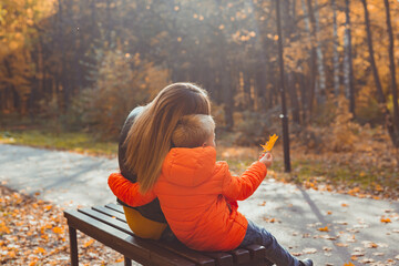 Single parent mother and child boy in the autumn in park sit on bench. Fall season and family concept.