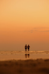 a couple of people at sunset. silhouettes stretching into the distance against the background of the sunset orange sky. beautiful view of the sea or lake. the beach and a beautiful view of nature