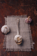 Some garlic bulbs on sackcloth, wooden table. Spicy vegetable, piquant flavouring, organic food, healthy eating, cooking ingredient. Vertical shot