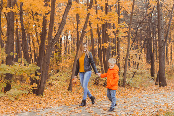 Fototapeta premium Mother and son walking in the fall park and enjoying the beautiful autumn nature. Season, single parent and children concept.