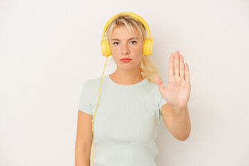 Young Russian woman listening to music isolated on white background standing with outstretched hand showing stop sign, preventing you.