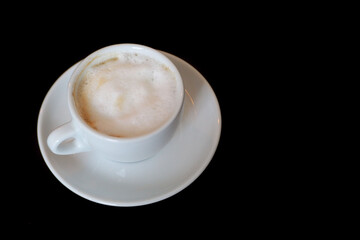 a natural cappuccino in a white cup and saucer stands on a black table. side view