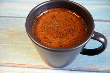 natural black coffee in a dark mug stands on a blue wooden table. side view