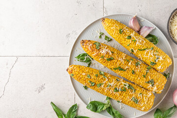 Grilled corn on the cob with butter, parmesan cheese and basil in a plate on stone background. top...