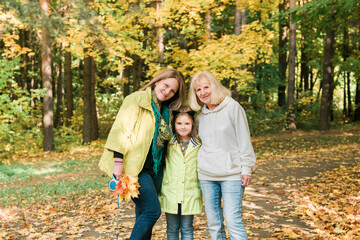 Fototapeta premium Portrait of three generations of happy beautiful woman looking at camera, hugging and smiling in autumn nature
