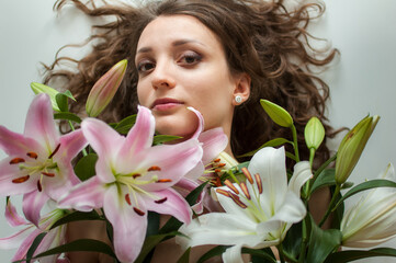 Top view of beautiful woman lying on the table with perfect bouquet of beautiful lilies, female portrait concept