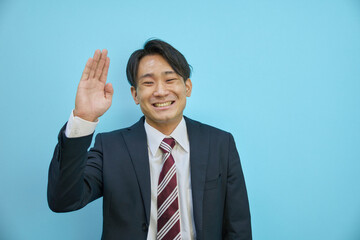 笑顔で手を挙げるスーツを着た日本人男性