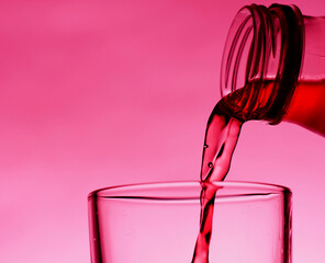 A red drink is poured into a transparent glass from a bottle.