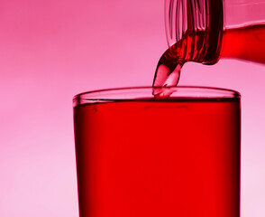 A red drink is poured into a transparent glass from a bottle.
