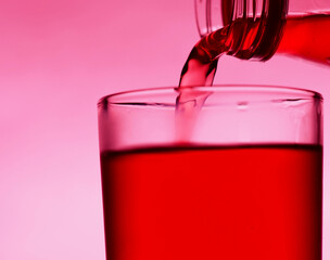A red drink is poured into a transparent glass from a bottle.