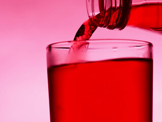 A red drink is poured into a transparent glass from a bottle.