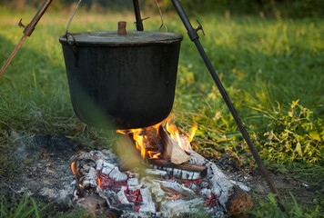 Dark big pot or cauldron, cooking pan with boiling water inside above the fire somewhere in the park or mountains, camping concept