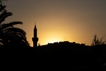 Dark silhouette of a mosque with a tall minaret at sunset. (Urfa, Turkey.)