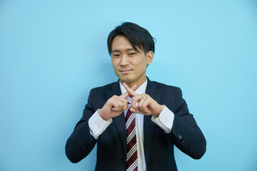 青背景の前でバツを作る日本人ビジネスマン