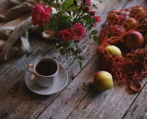 A cup of coffee on a wooden background, apples in a bag are on the table.