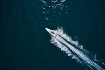 Speed boat faster movement on the water top view. Speedboat movement on the water. Speedboat wave speed water. Large white boat driving on dark water. Speedboat on dark blue water aerial view.