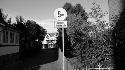 Grayscale shot of a caution street sign in German, outdoors during daylight